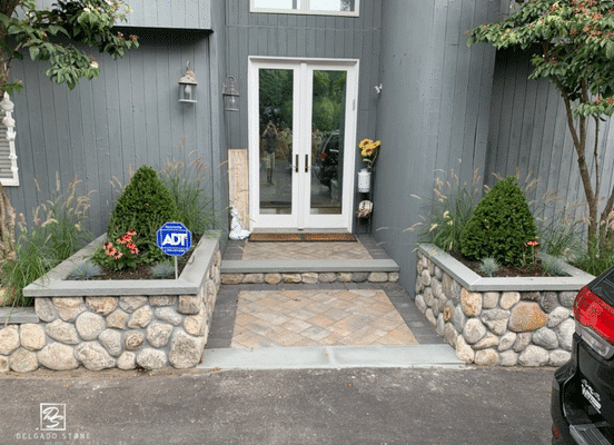 Photo of Cedar Creek River Rounds Natural Stone installed on entry columns and landscape walls at a residential entrance.