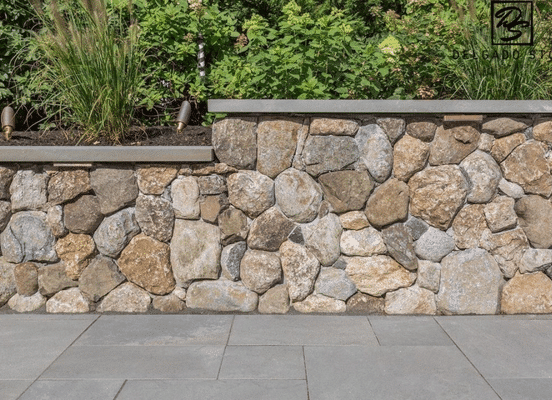 Photo of Old New England Rounds Natural Thin Stone Veneer installed on a natural stone retaining wall.