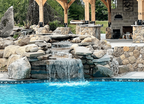 Photo of Old New England Rounds Natural Thin Stone Veneer installed around a pool waterfall and outdoor living area.