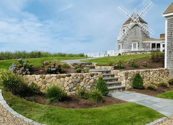 Curved stone retaining wall with integrated stone steps in a landscaped backyard setting.