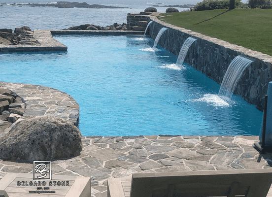 Photo of American Mist Mosaic stone veneer by Delgado Stone surrounding a luxury pool and outdoor living space, featuring natural stone veneer walls, patios, and coastal backyard design.
