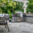 Unilock Rivercrest® Wall outdoor kitchen with a built-in grill, dining area, and covered patio.